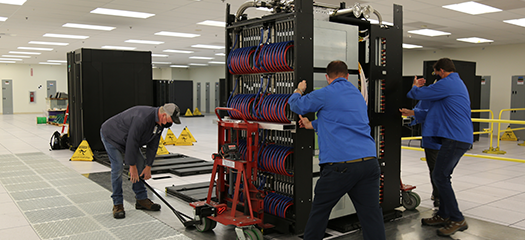 three people install an early access system rack in the machine room