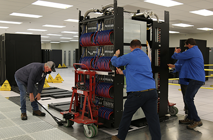 three people install an early access system rack in the machine room