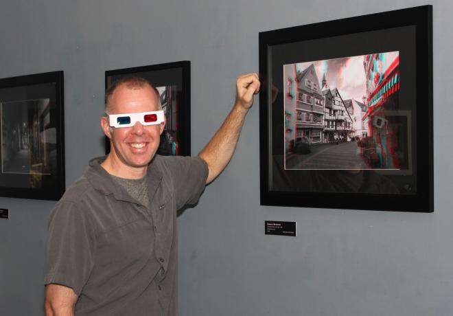 Kirk Sylvester wears 3D glasses next to his photograph of a street scene