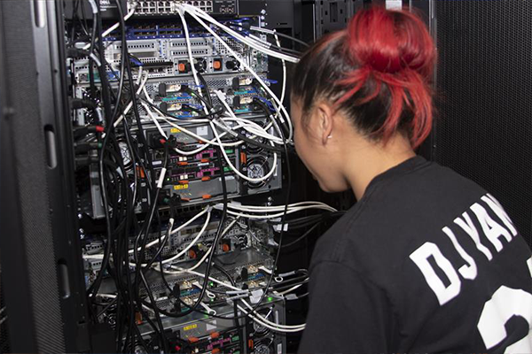 A student views the cables inside an HPC cluster's cabinet