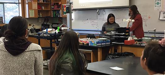 Marisa works with a student on a computer at the front of the class