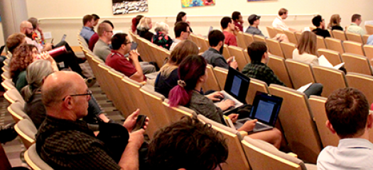people in chairs in an auditorium listening to a speaker