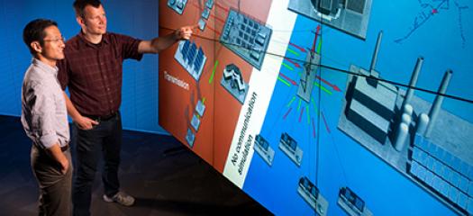 two scientists stand next to a large wall onto which a power grid diagram is projected