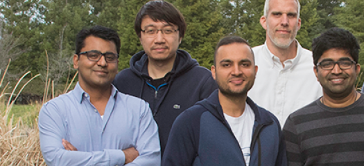 Five researchers stand in a group in front of trees and tall grasses