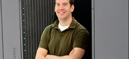 Mid-career, white researcher with arms crossed in from of large gray computer rack