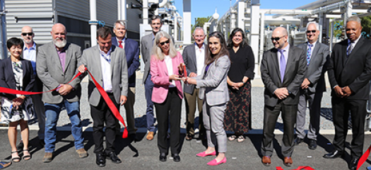 13 people cut a red ribbon in front of the new building