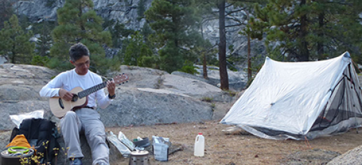 Brian Gunney playing guitar at a campsite