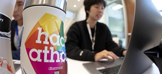 Summer interns work on their hackathon projects. A water bottle with a hackathon sticker on it is in the photo’s foreground.