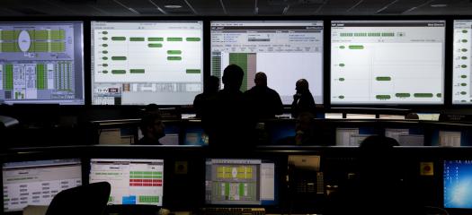 Silhouettes of researchers monitoring many screens of data.