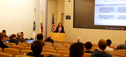 Judy Hill presents at a lectern to an auditorium of people