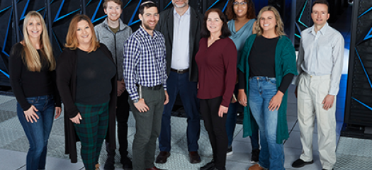 nine people stand as a group in front of the Sierra supercomputer