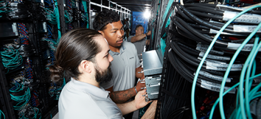 looking down a row of racks with exposed wires, three people install components of El Capitan
