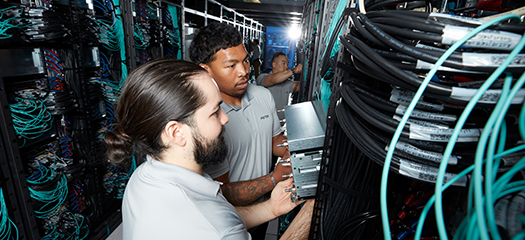 ooking down a row of racks with exposed wires, three people install components of El Capitan