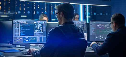four people at computer workstations in a dark blue server room