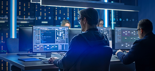 four people at computer workstations in a dark blue server room