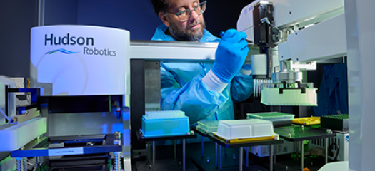 a scientist in PPE performs an experiment with an apparatus labeled as Hudson Robotics