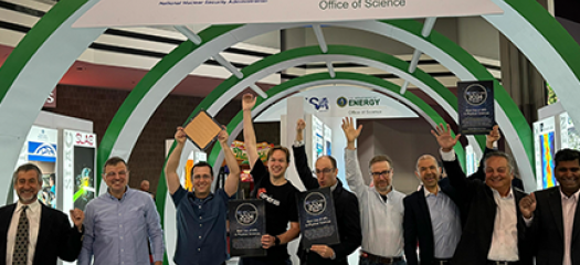 nine people pose in jubilation at the DOE exhibit booth