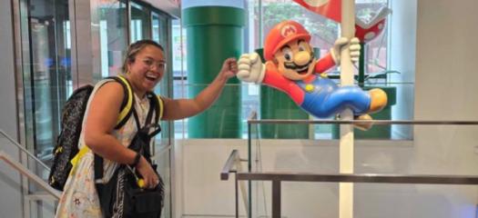 Sunshine inside giving a fist bump to a Mario Bros statue hanging off a vertical pole 