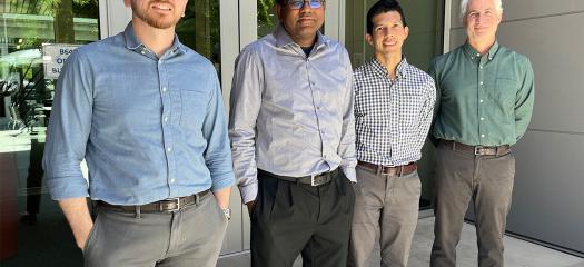 four people stand outside a building with glass windows