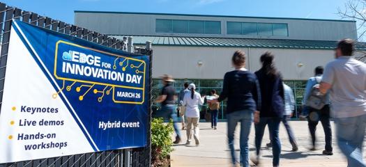 several people walk into a building past a sign for aiEDGE Innovation Day