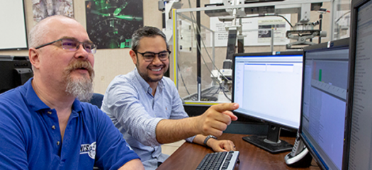 Jorge works with another person on a desktop computer