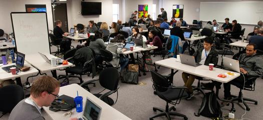 wide shot of the room with hackathon teams working at tables