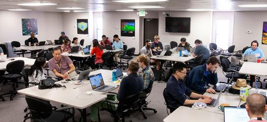 teams work at laptops and tables in the main hackathon room
