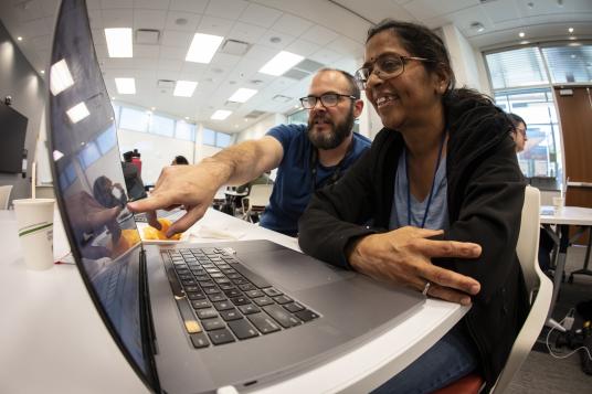 Two people look at a laptop. One is pointing at something on the screen.