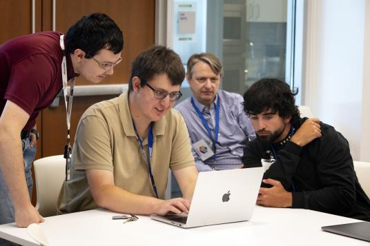 Four people sitting around a laptop.