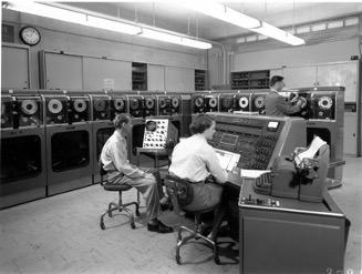 black-and-white photo showing a man and two women working at early computers