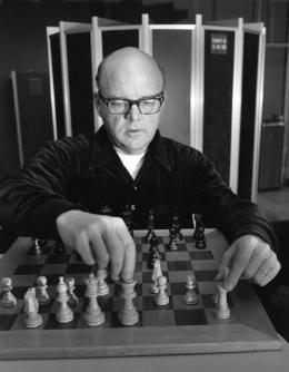 Black-and-white photo of Harry Nelson facing the camera and moving pieces on a chessboard