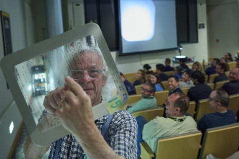 Close up of man holding a transparency with an auditorium full of people behind him