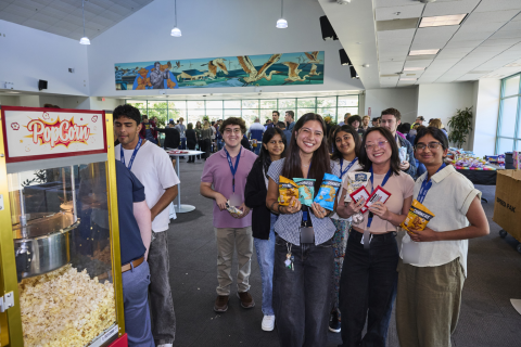 A group of students are in the Lab’s cafeteria standing next to a popcorn machine.   