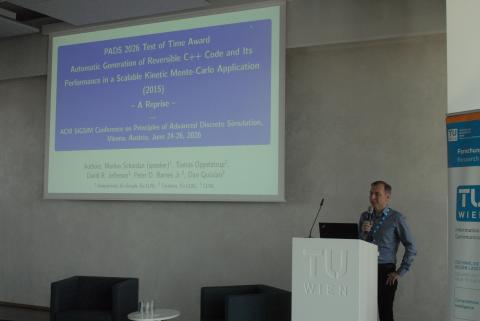 Markus stands behind a podium with a large screen behind him on which is projected the title slide from his talk originally given 10 years ago.  