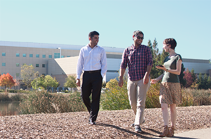three researchers walk around the Lab's lake with the HPC building in the background