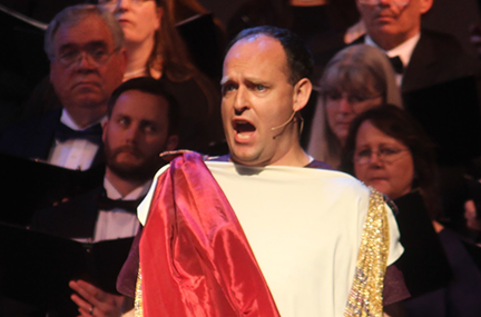 Jarom Nelson performing in Roman dress in front of a choir of formally dressed singers