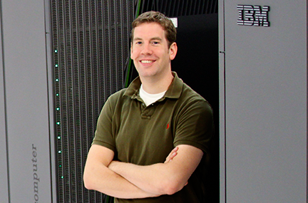 Mid-career, white researcher with arms crossed in from of large gray computer rack