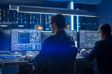 four people at computer workstations in a dark blue server room