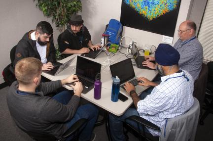 A group of people sitting around a table, interacting, and working on laptops