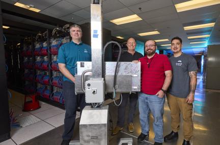 Four people pictured with a large piece of computer equipment smiling at the camera 