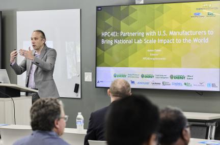 Man presenting at a lecturn with giant slide behind him about US Manufacturing and HPC