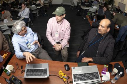 three people discussing their work with laptops