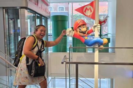 Sunshine inside giving a fist bump to a Mario Bros statue hanging off a vertical pole 