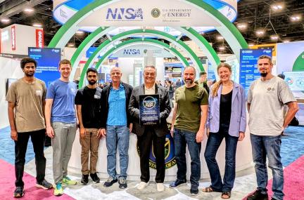 A group of award winners stands in the DOE booth at SC25