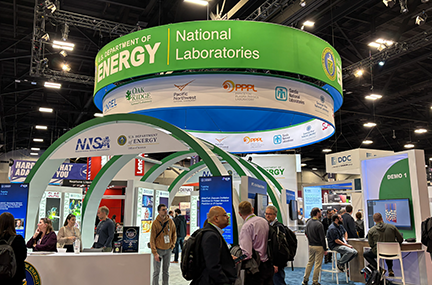 people clustered in and around the Department of Energy booth, which consists of large green and white circular structures with a demo station on the right side