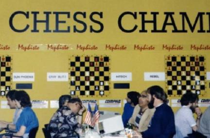  several chess players seated at tables during a competition, in front of competition-related signs on a yellow wall