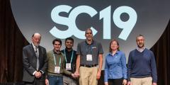six people stand in front of an SC19 sign