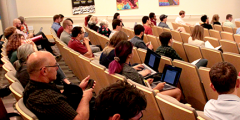 people in chairs in an auditorium listening to a speaker
