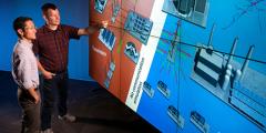 two scientists stand next to a large wall onto which a power grid diagram is projected