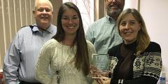 four people in an office holding an award